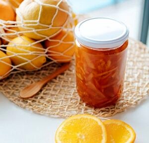 sok pomarańczowy w słoiku na stole na tle pomarańczy w koszyku